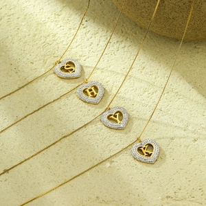 Gold heart pendant necklaces with zircon letters S H Y K on a minimalist stone background