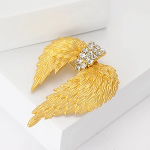 Golden alloy wing brooch with rhinestones displayed on white geometric pedestal