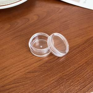 Detailed macro view of the small clear plastic circular jewelry storage jar on wood