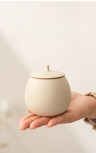 Close-up of compact beige ceramic tea canister held in hand to show portable small size