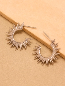 Detailed close-up of silver sunflower ray sunburst C-shaped earrings on stone background