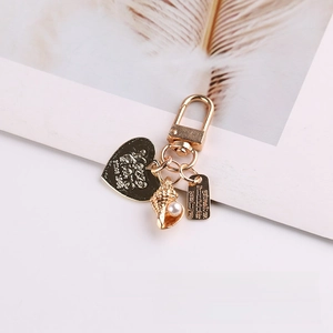 Detailed close-up of golden keychain pendant with heart tag and pearl conch charms
