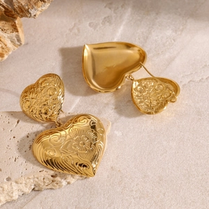 Macro detail of golden heart earrings with intricate floral relief on stone background