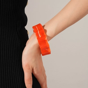 Close-up of bright orange resin wide bangle with wavy texture worn on a wrist