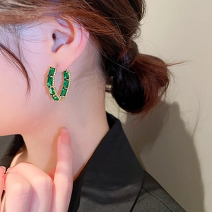 Detailed close-up of a golden geometric hoop earring featuring inlaid green emerald-style zircons