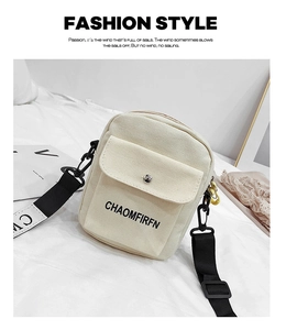 Flat lay of cream canvas crossbody bag with black lettered straps on fabric background