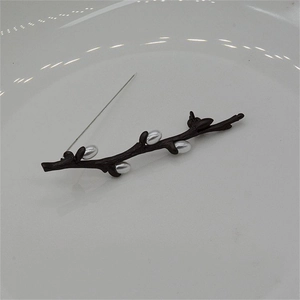 Elegant plum blossom branch brooch with brown lacquer and pearls on a white plate