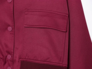 Detail of dark red jacket featuring buttoned pocket flap and ribbed elastic hemline texture