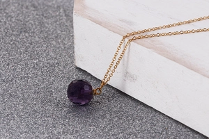Close-up of faceted purple crystal sphere pendant with a delicate gold chain