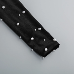 Détail de perles blanches sur manche en satin noir d'une robe de soirée sexy