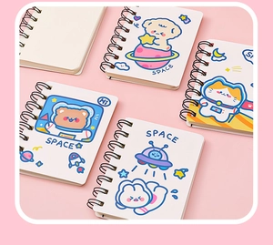 Close-up of four mini spiral notebooks with cute cartoon astronaut animal illustrations