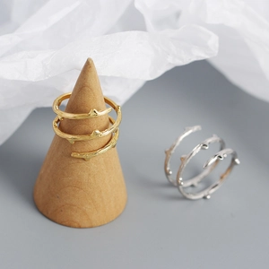 Detail of gold and silver branch-textured open rings displayed on minimalist stands