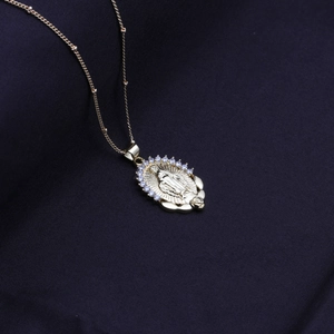 Detailed view of gold Virgin Mary pendant with crystals on blue silk background