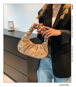 Detail view of a beige pleated dumpling shoulder bag styled with a minimalist outfit