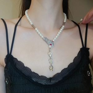 Detail of pearl necklace featuring a diamond-encrusted snake head pendant with red eyes