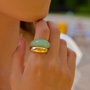 Dettaglio di un anello in metallo dorato e un anello in pietra verde su un dito