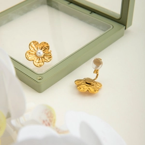 Détail de boucles d'oreilles clips fleurs dorées avec perle blanche sur support
