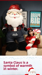 Detail of giant Santa plush in plaid shirt and denim overalls with Merry Christmas embroidery