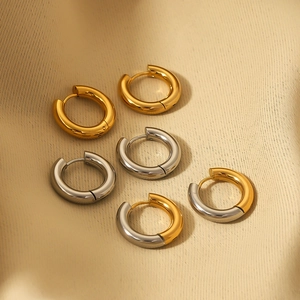 Three pairs of stainless steel hoop earrings in gold, silver, and bicolor on beige fabric