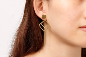 Close-up of golden geometric hollow diamond earrings worn by a model in a minimal style