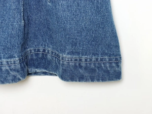 Makroaufnahme des doppelt genähten Saums und der blauen Denim-Struktur eines taillierten Hemdes