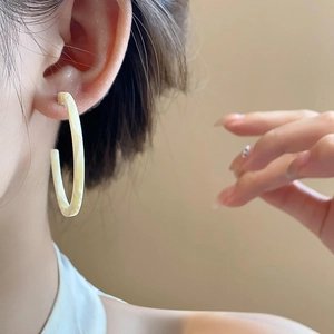 Close-up of retro ivory resin C-shape earring with marble texture on model's ear