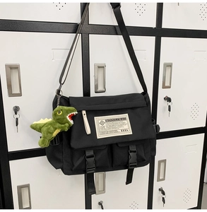Detail of black messenger bag with green dinosaur plush pendant on a storage locker
