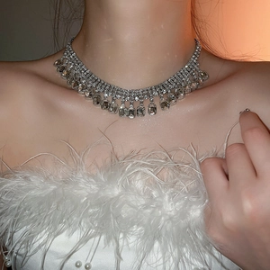 Gros plan d'un collier à pompons argenté et cristaux carrés sur un mannequin avec plumes