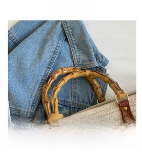 Detail of woven tote bag featuring natural bamboo handles and reinforced leather stitching