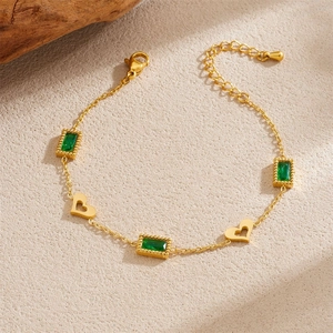 Detail of gold chain bracelet featuring emerald stones and hollow heart charms on stone