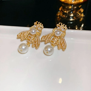 Détail de boucles d'oreilles abeille dorées avec perles sur assiette blanche et fond sombre