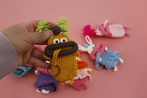 Handheld view of colorful crochet sausage mouth key cases with metallic rings