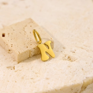 Detailed close-up of polished gold letter N pendant on minimalist textured stone background