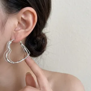 Detail shot of heart-shaped large silver hoop earrings with textured wavy surface