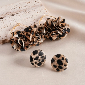Close-up of leopard print fabric flower hoop earrings and studs on beige silk background
