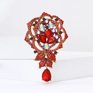 Elegant gold flower brooch with red crystals and teardrop pendant on white background