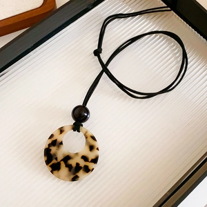 Close-up of leopard print hollow circular resin pendant on a black cord necklace