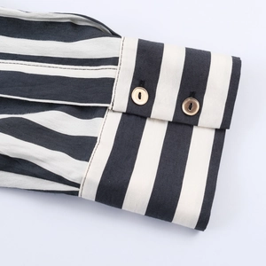 Detailed close-up of striped shirt cuff with black and white patterns and gold buttons