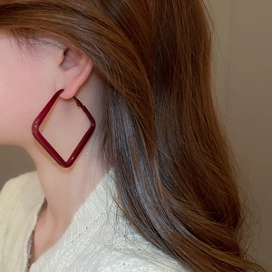 Detail of a woman wearing large square deep red enamel hoop earrings in a stylish pose