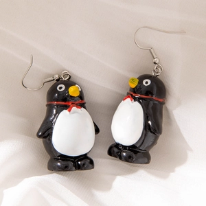 Detailed close-up of cartoon penguin earrings with red bowties on white fabric