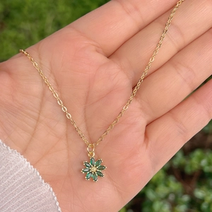 Gros plan détaillé d'un collier doré avec un pendentif fleur en zircon vert tenu en main