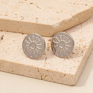 Close-up of silver round stud earrings with embossed dots on beige travertine stone