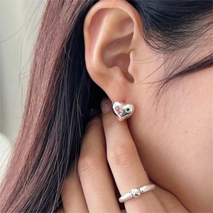 Detail of model wearing 925 silver heart stud earrings with pink and green stones and a bead ring