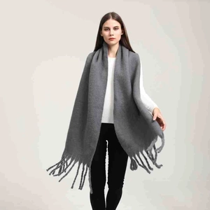 Dettaglio della sciarpa in maglia grigia con texture morbida e nappe decorative ai bordi