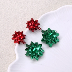 Detailed view of festive red and green bow-shaped Christmas earrings on a white shell plate
