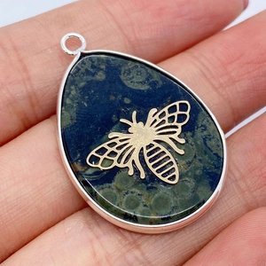 Macro shot of dark green teardrop stone pendant with a gold bee and silver metal edging