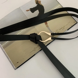 Fashionable black thin leather belt with golden horseshoe buckle on a white background