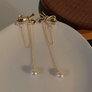 Detail of golden bow tassel earrings with white pearls on elegant ceramic plate