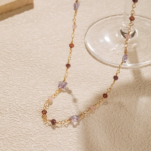 Detail of bohemian necklace featuring purple butterfly bead and faceted stones on gold chain