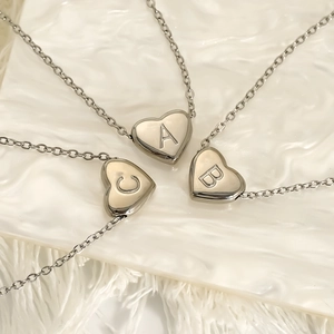 Three silver stainless steel heart pendant necklaces with A, B, C letters on a white tray